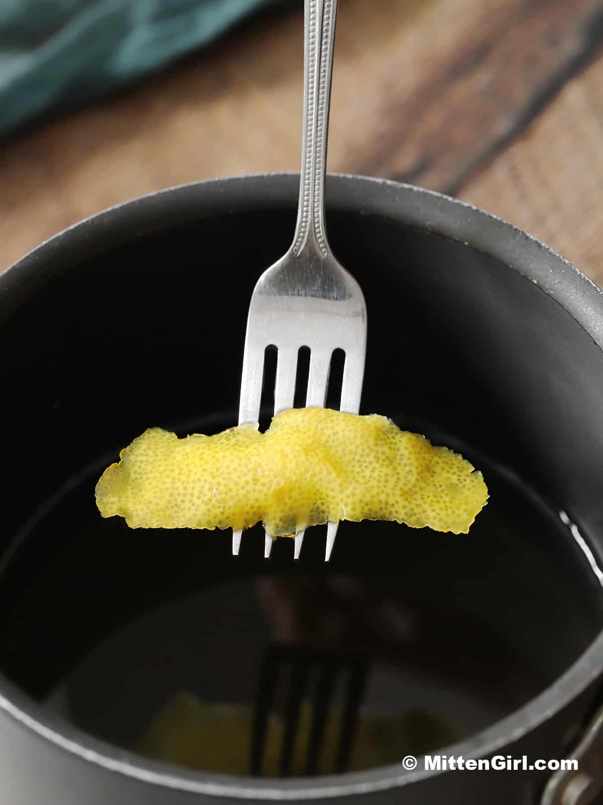 A fork removing a piece of lemon peel from a small pot. 
