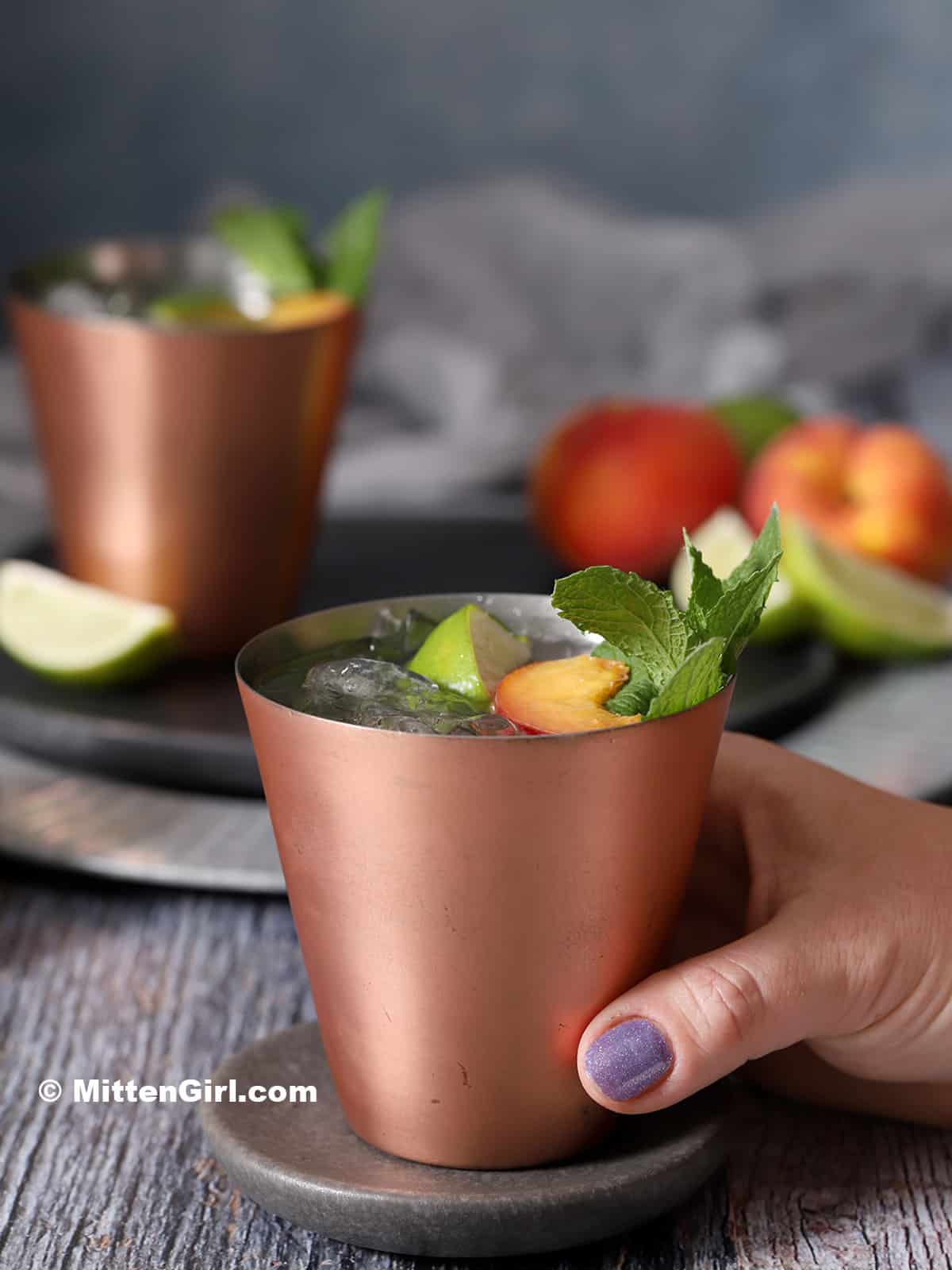 A hand picking up a copper cup of peach Moscow Mule. 