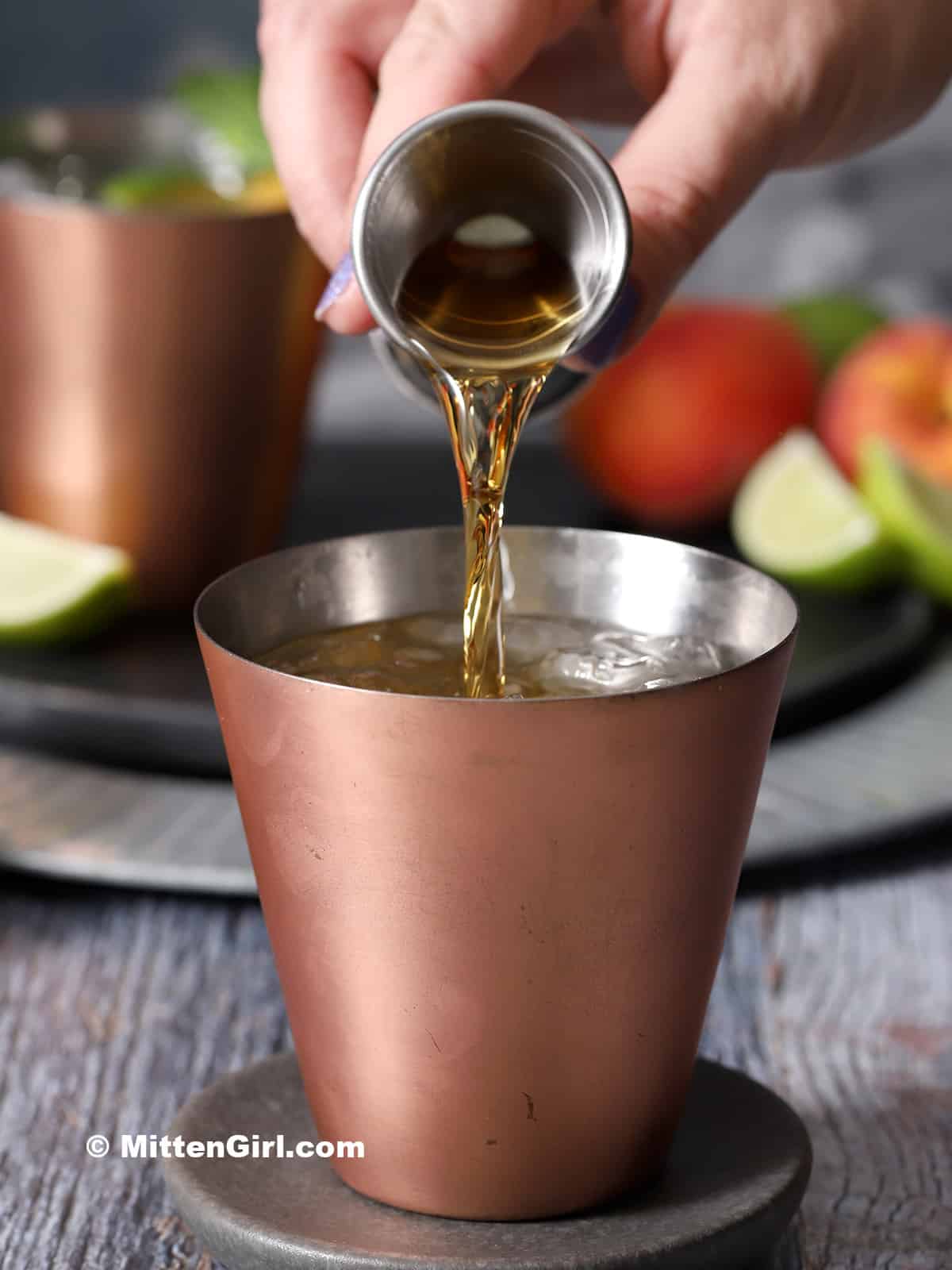 Bourbon being poured into a copper cup with lime and ginger beer. 
