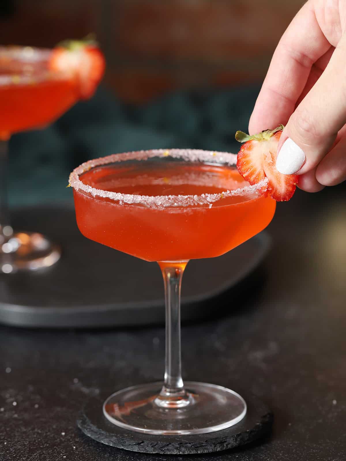 A hand garnishing a glass of strawberry lemon drop martini with a fresh strawberry. 