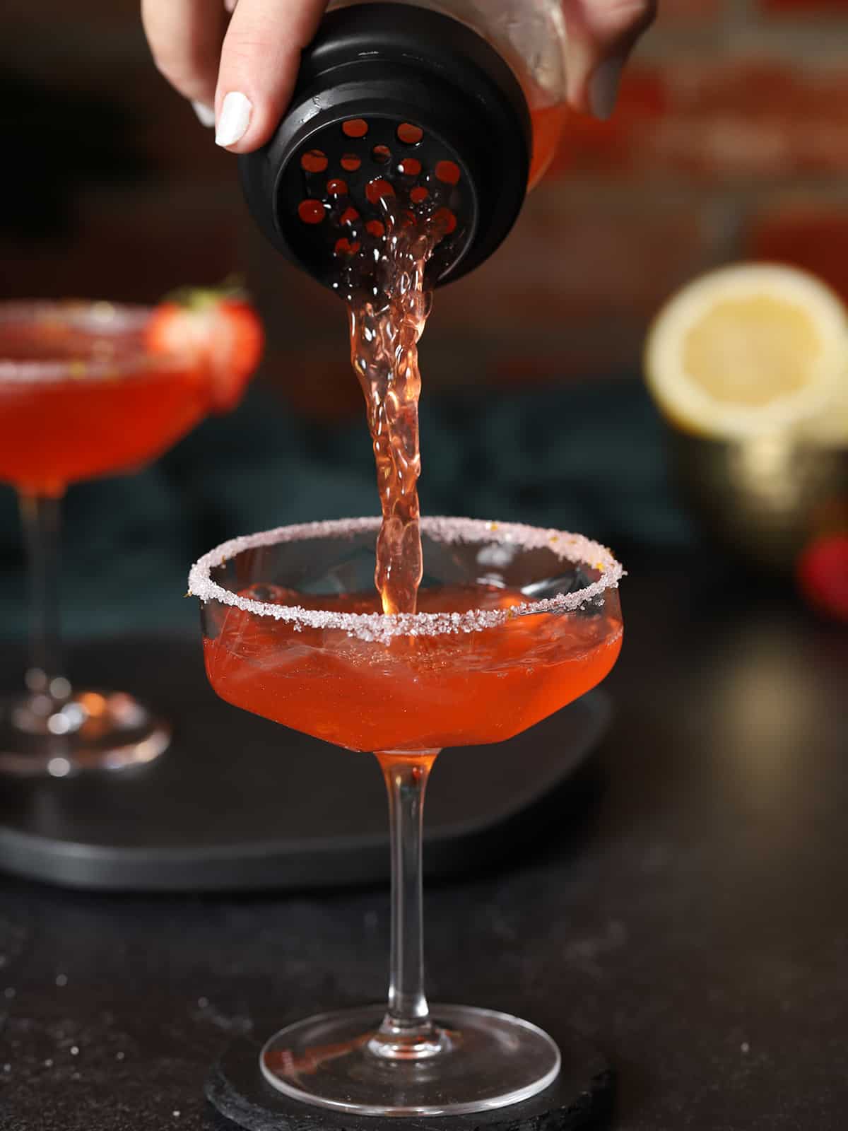 Strawberry lemon drop cocktail being poured into a coupe glass. 