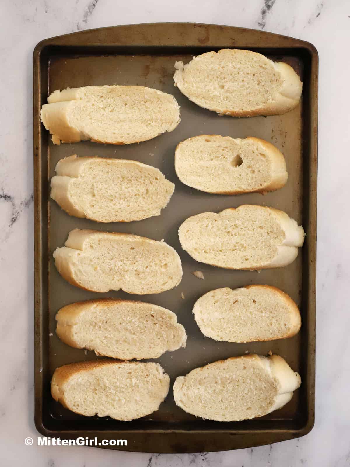Bread slices on a tray ready for the broiler. 