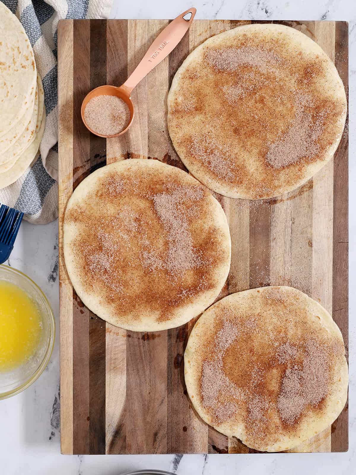 Tortillas on a cutting board covered in a thick layer of cinnamon sugar.