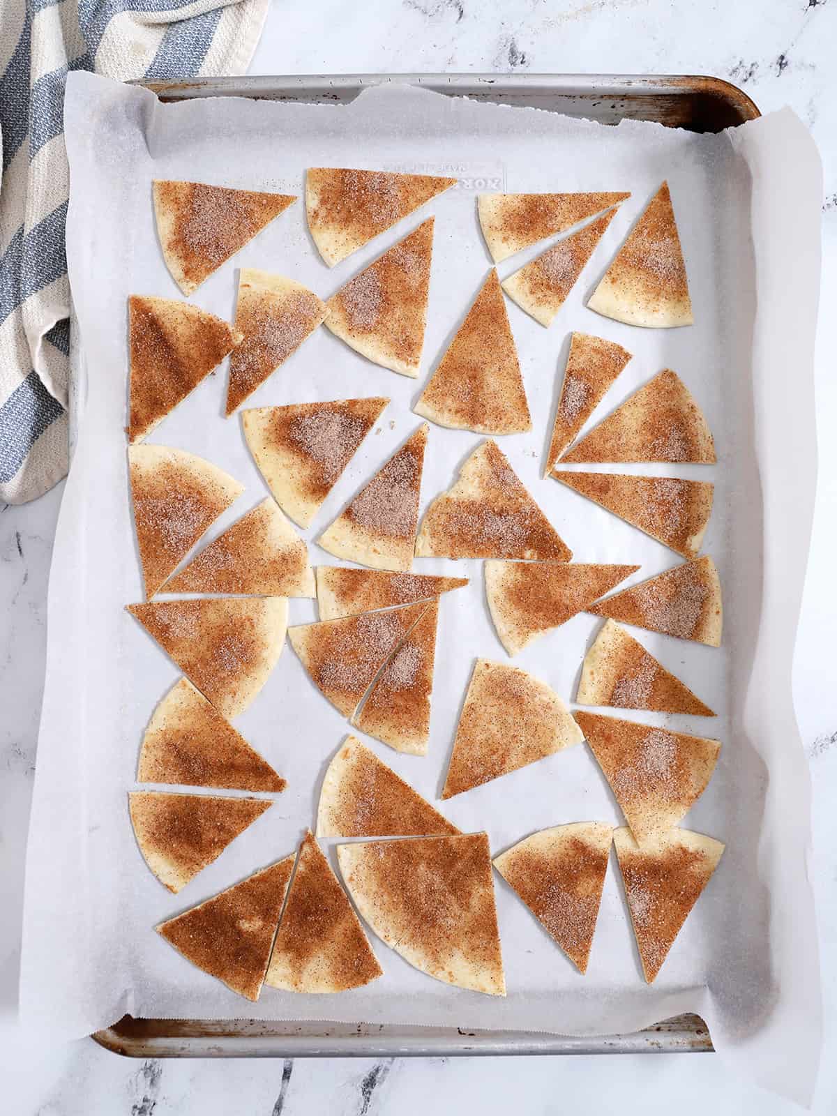 A sheet pan covered with parchment paper and triangles of cinnamon sugar tortillas, ready for the oven.