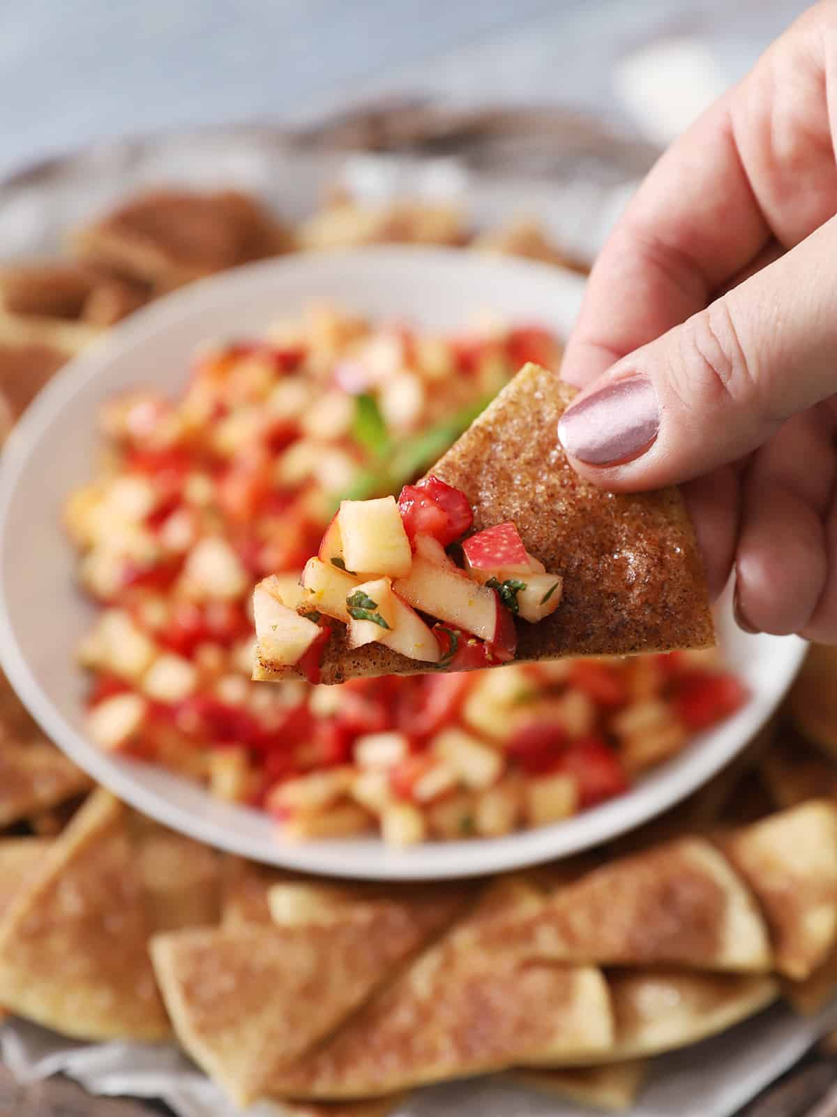 A hand holding a cinnamon tortilla chip with fresh fruit salsa on it.