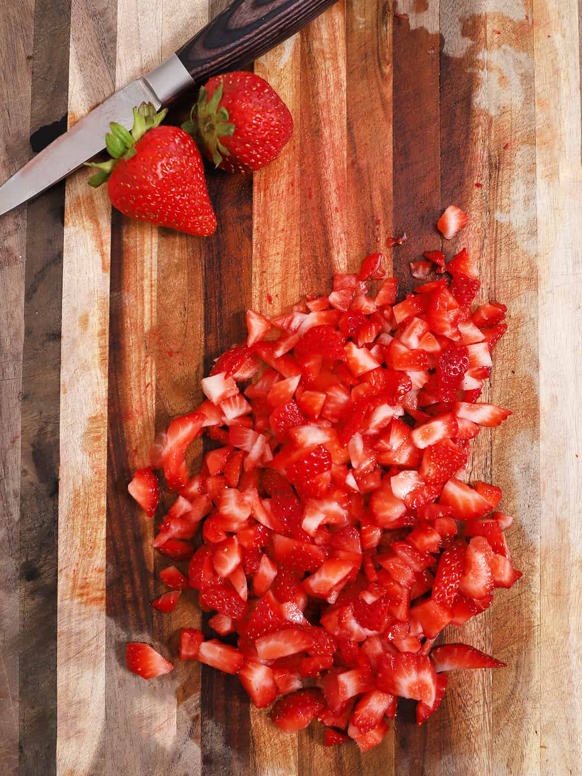 A cutting board full of diced strawberry pieces.