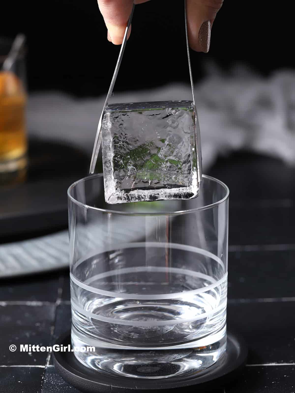 A large, clear ice cube being placed into a rocks glass. 