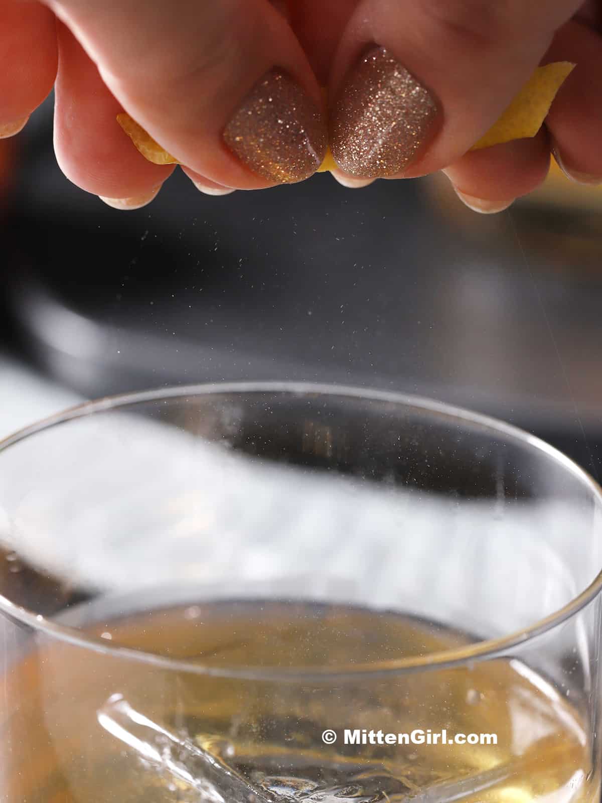 A hand squeezing a lemon peel over a glass of cocktail. 
