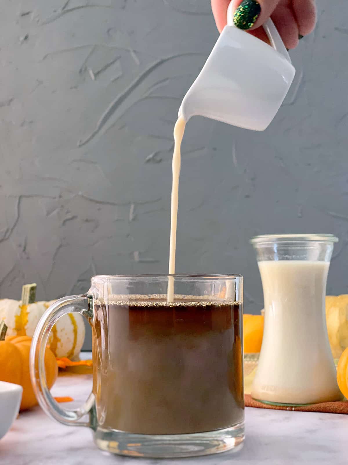 A hand pouring pumpkin spice creamer into a cup of coffee. 