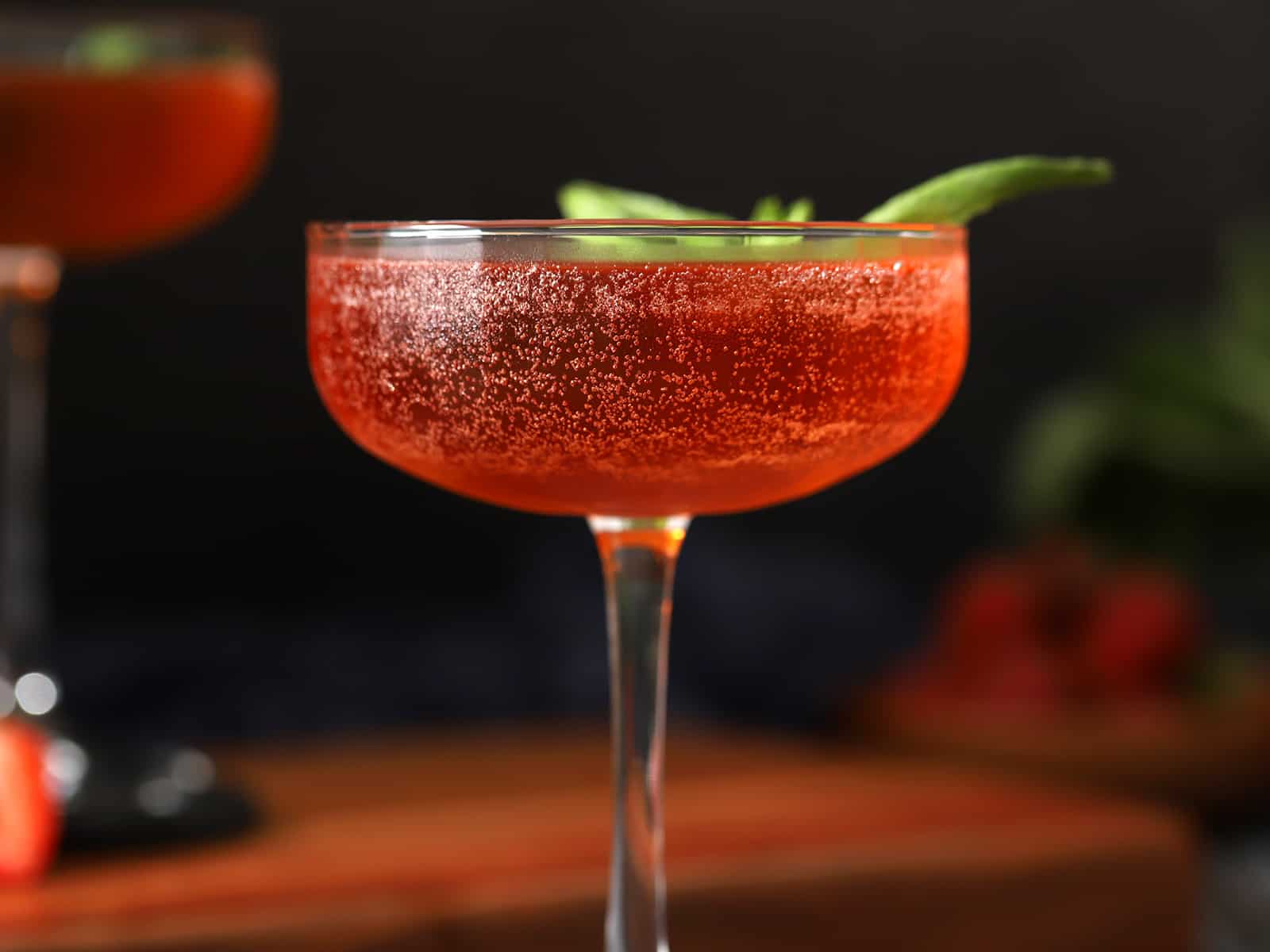A glass of strawberry basil cocktail garnished with a basil leaf.