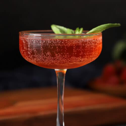A glass of strawberry basil cocktail garnished with a basil leaf.
