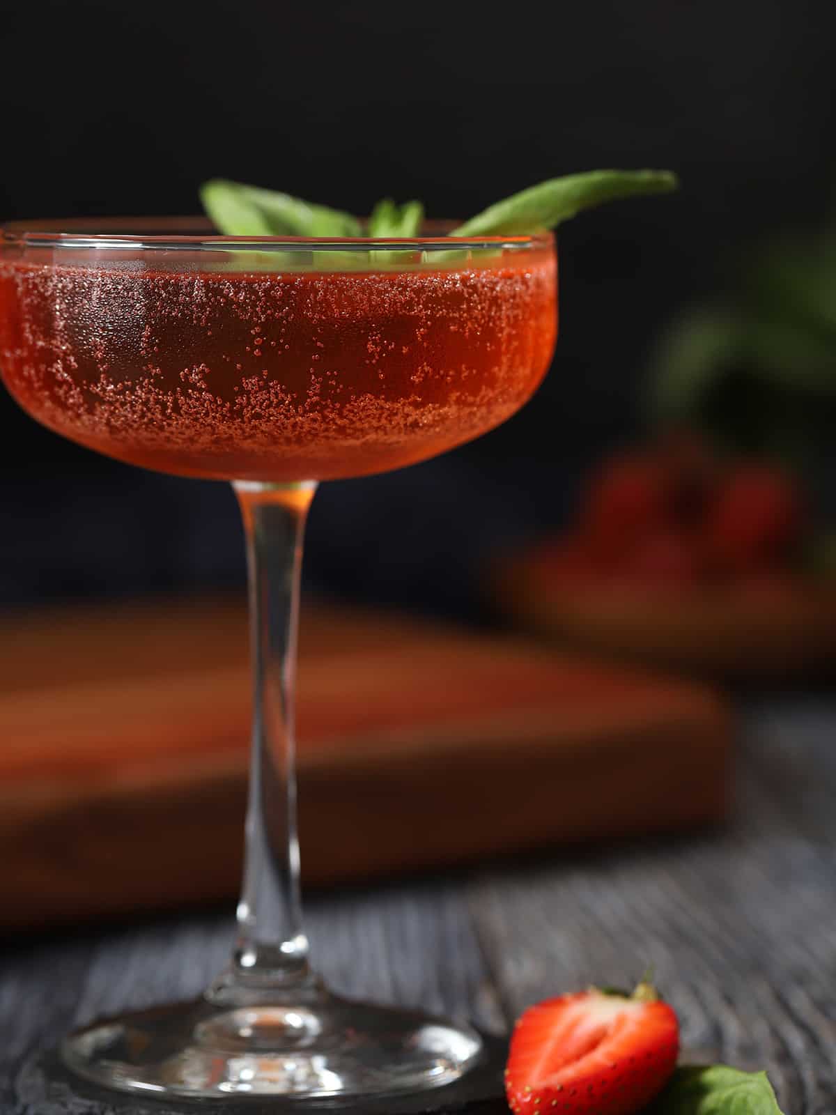 A glass of strawberry basil cocktail garnished with a basil leaf.