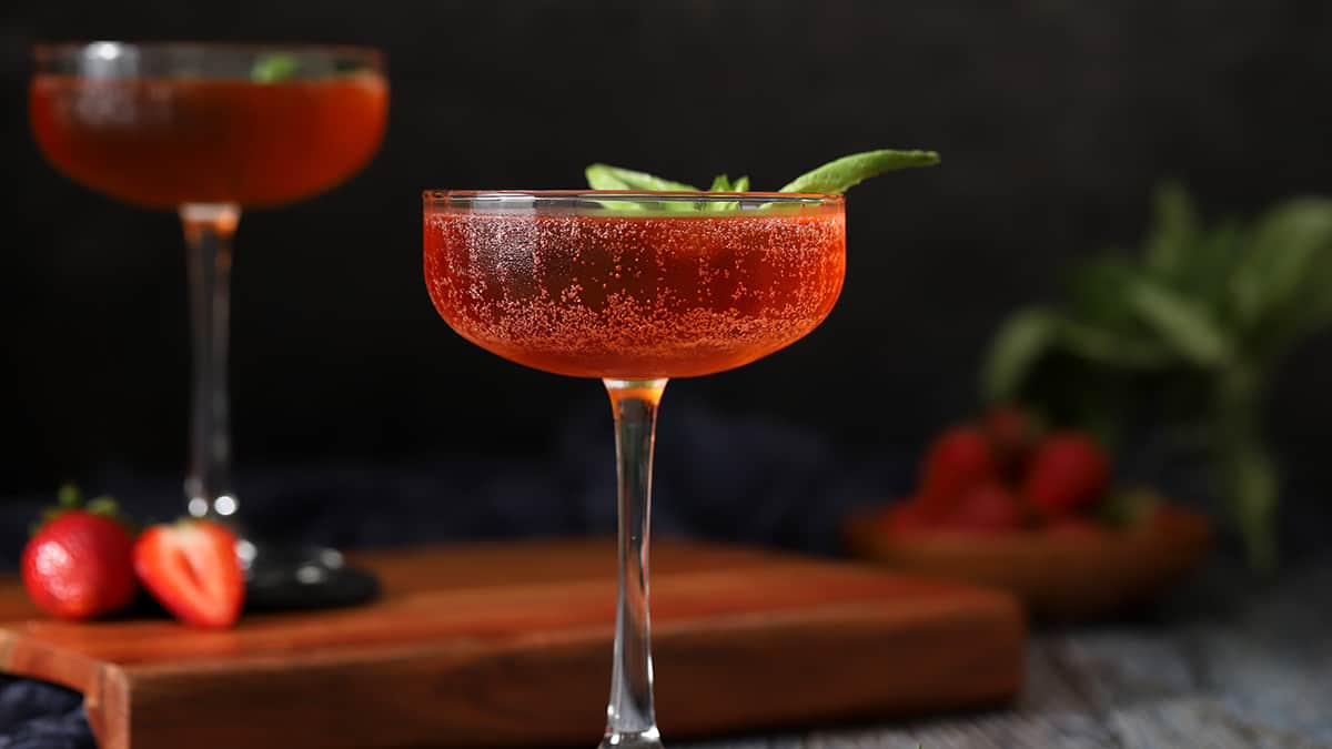 A glass of strawberry basil cocktail garnished with a basil leaf. 