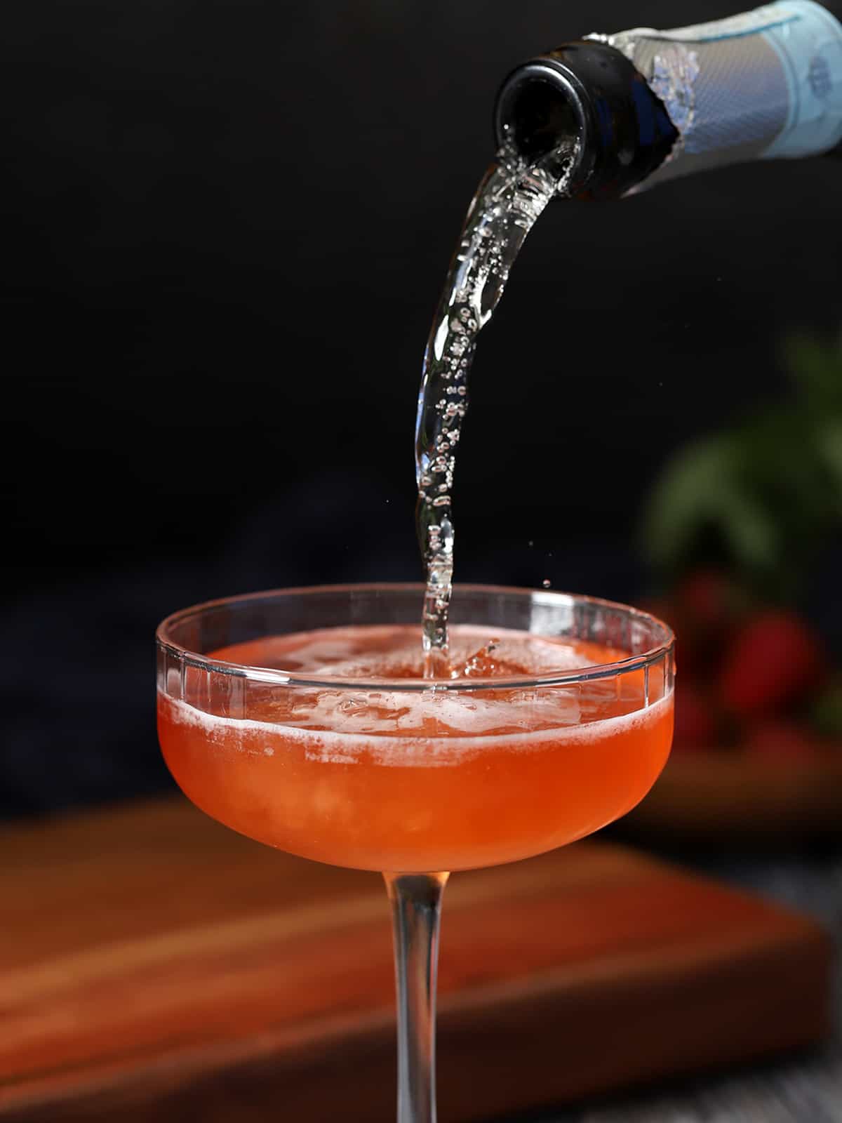 Prosecco being poured into a coupe glass of strawberry basil cocktail.