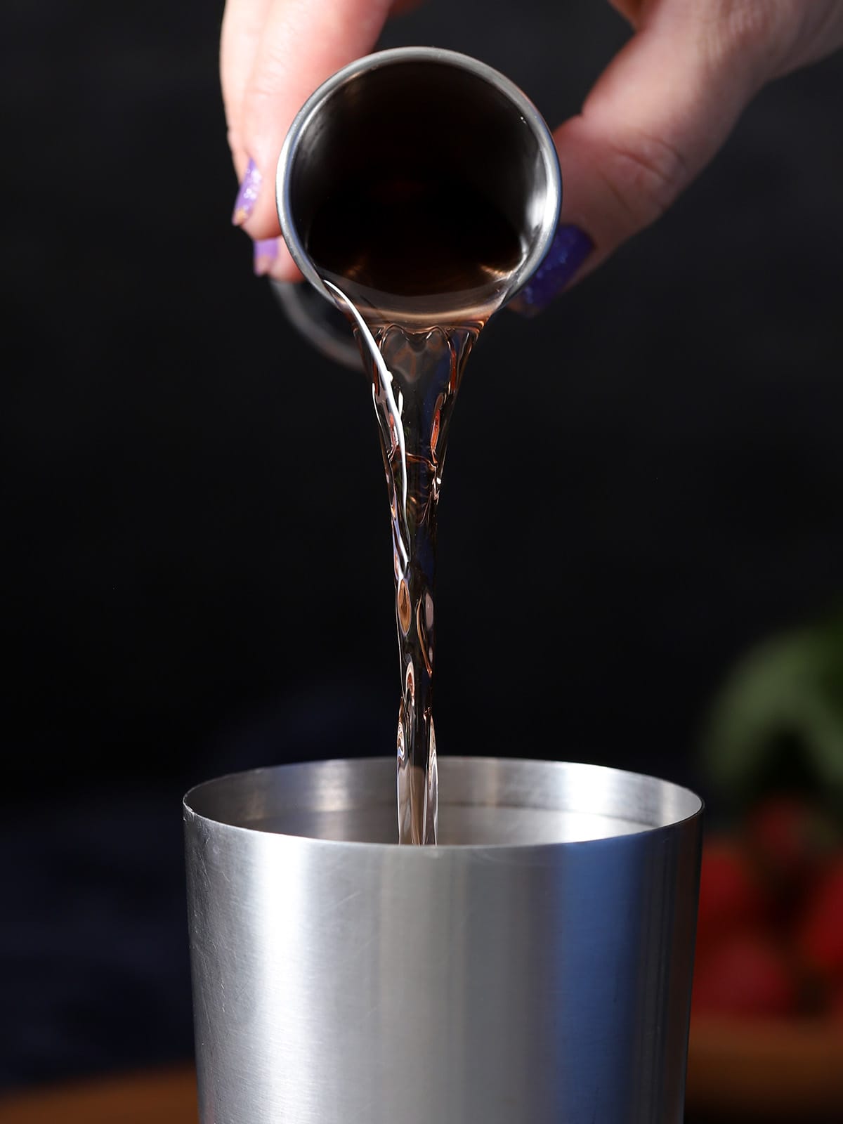 A hand pouring strawberry vodka into a cocktail shaker.