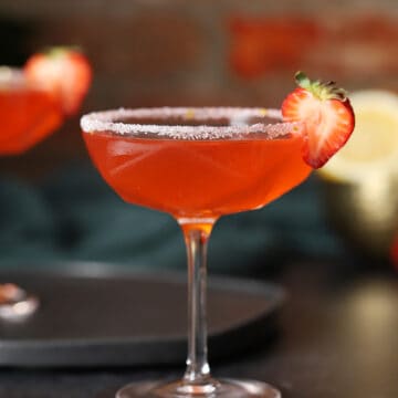 A coupe glass of strawberry lemon drop martini cocktail with a white sugar rim and strawberry slice garnish.