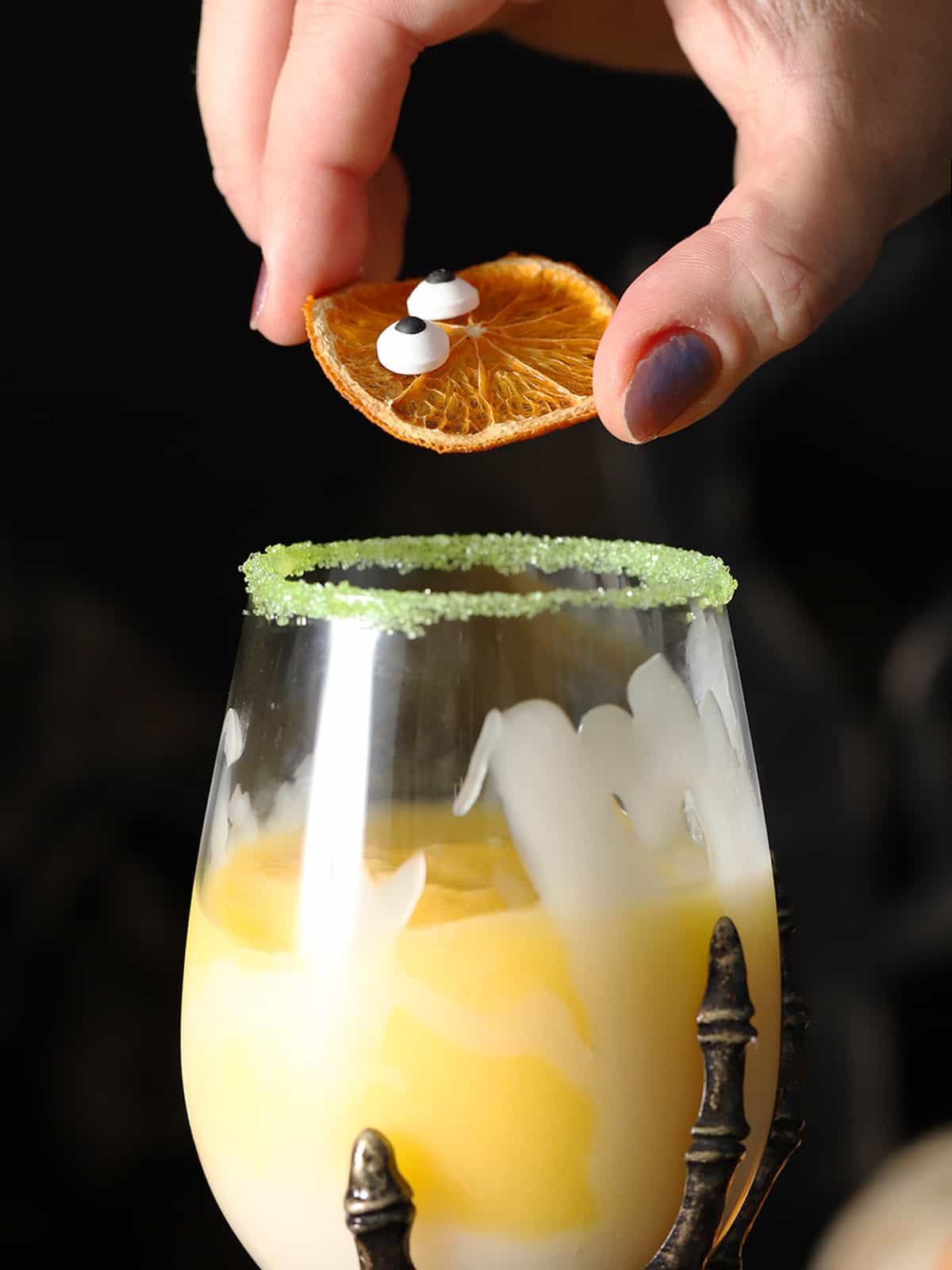 A hand placing a garnish into a non-alcoholic Halloween drink. 