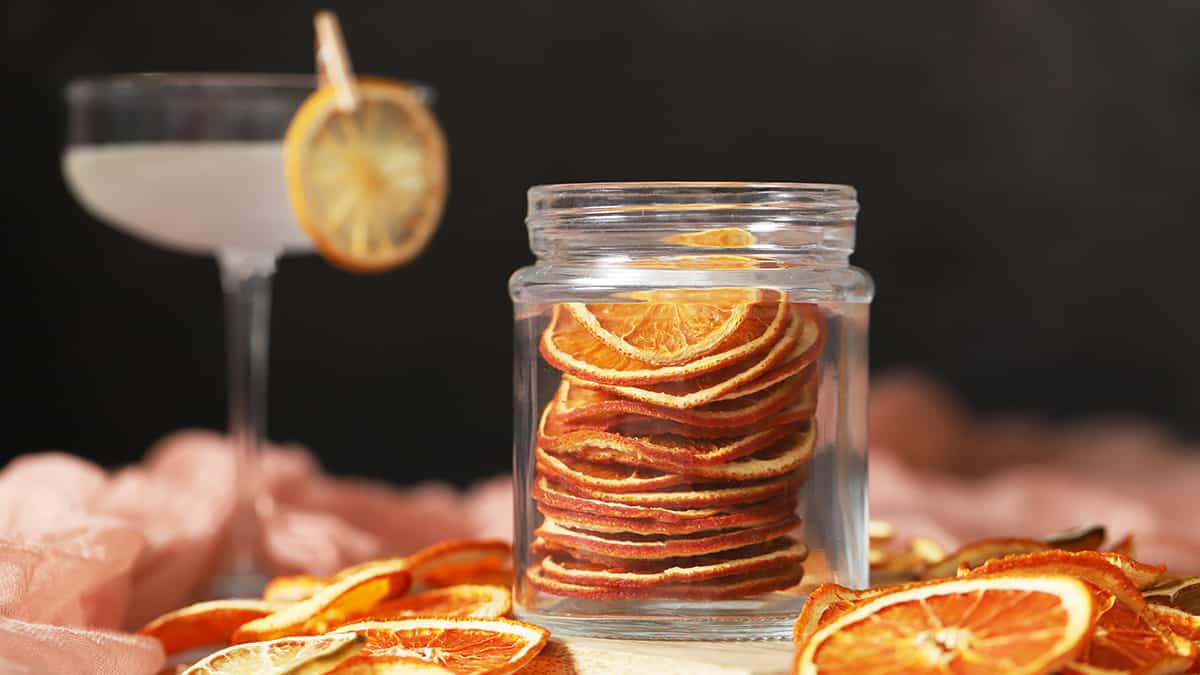A jar of oven dried orange slices, surrounded by more dehydrated citrus slices. 