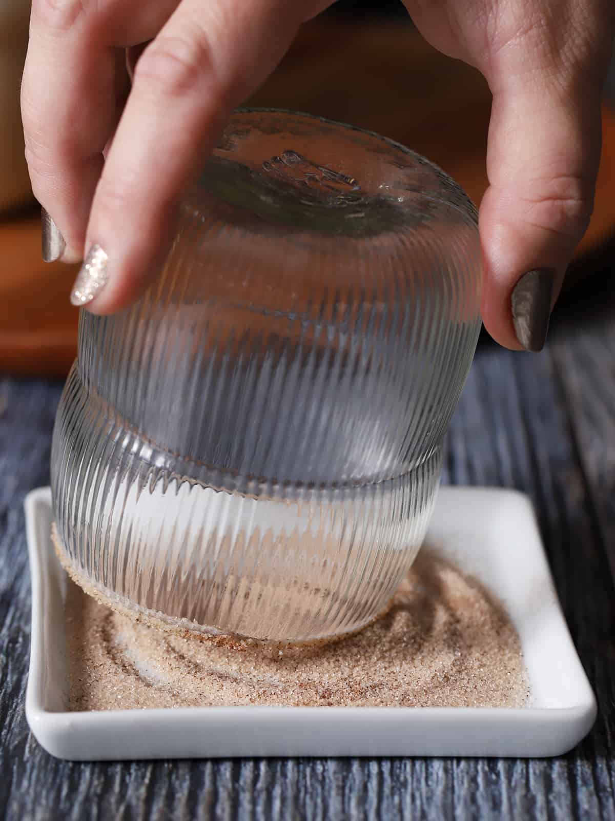 A hand dipping a glass into a cinnamon sugar mix. 