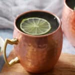A copper mug filled with moscow mule cocktail and a lime floating on top.