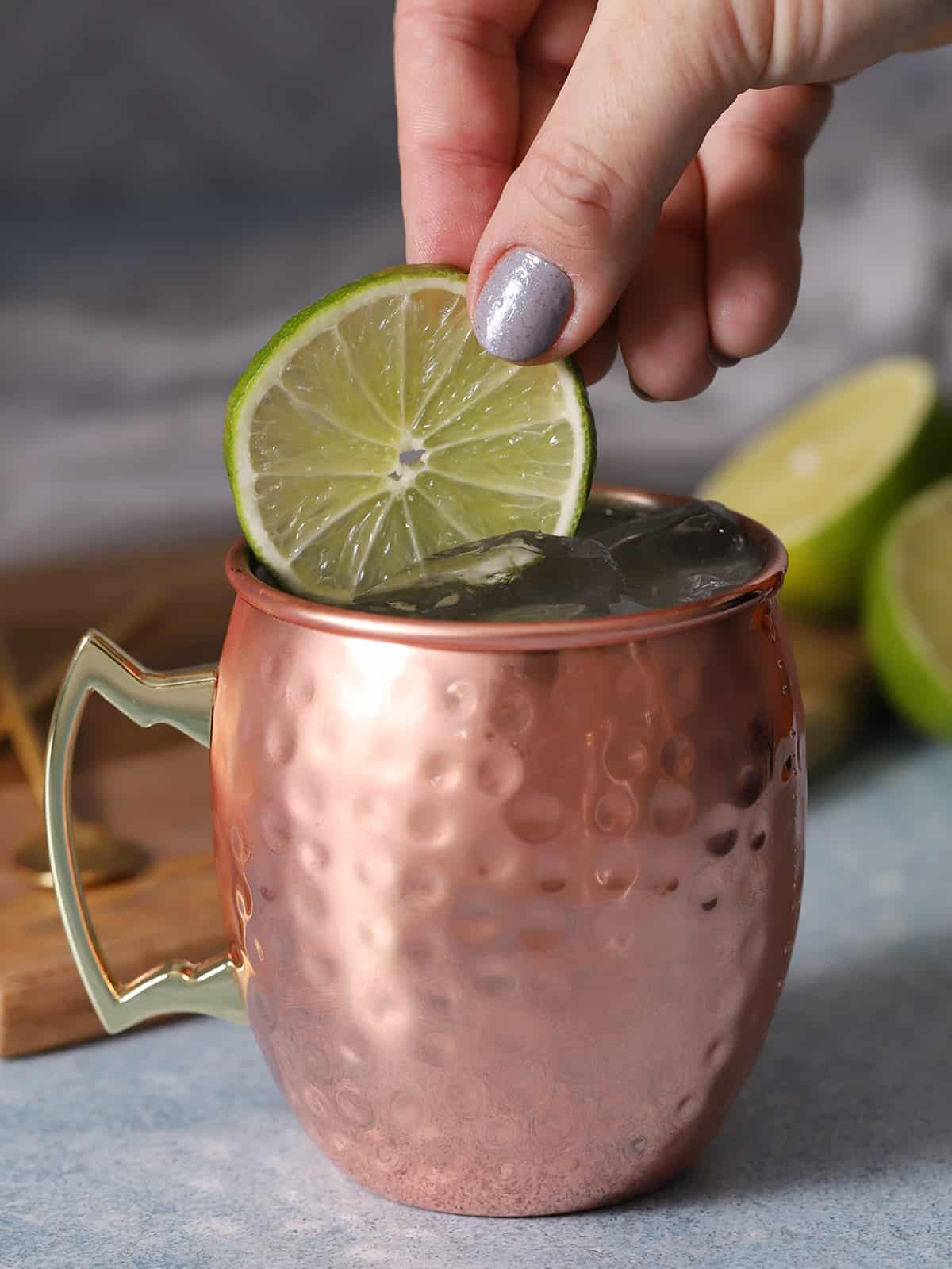 A hand garnishing a moscow mule drink with a slice of fresh lime. 