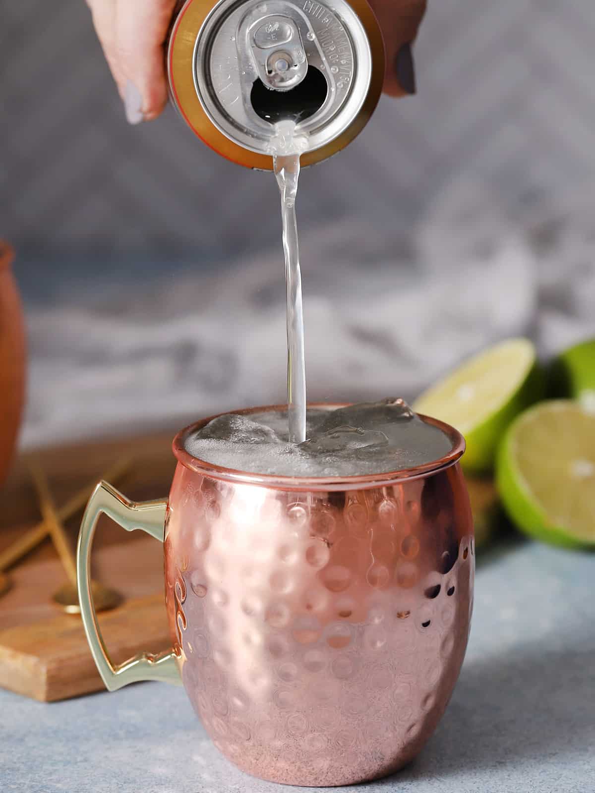 A hand pouring ginger beer into a copper moscow mule mug. 
