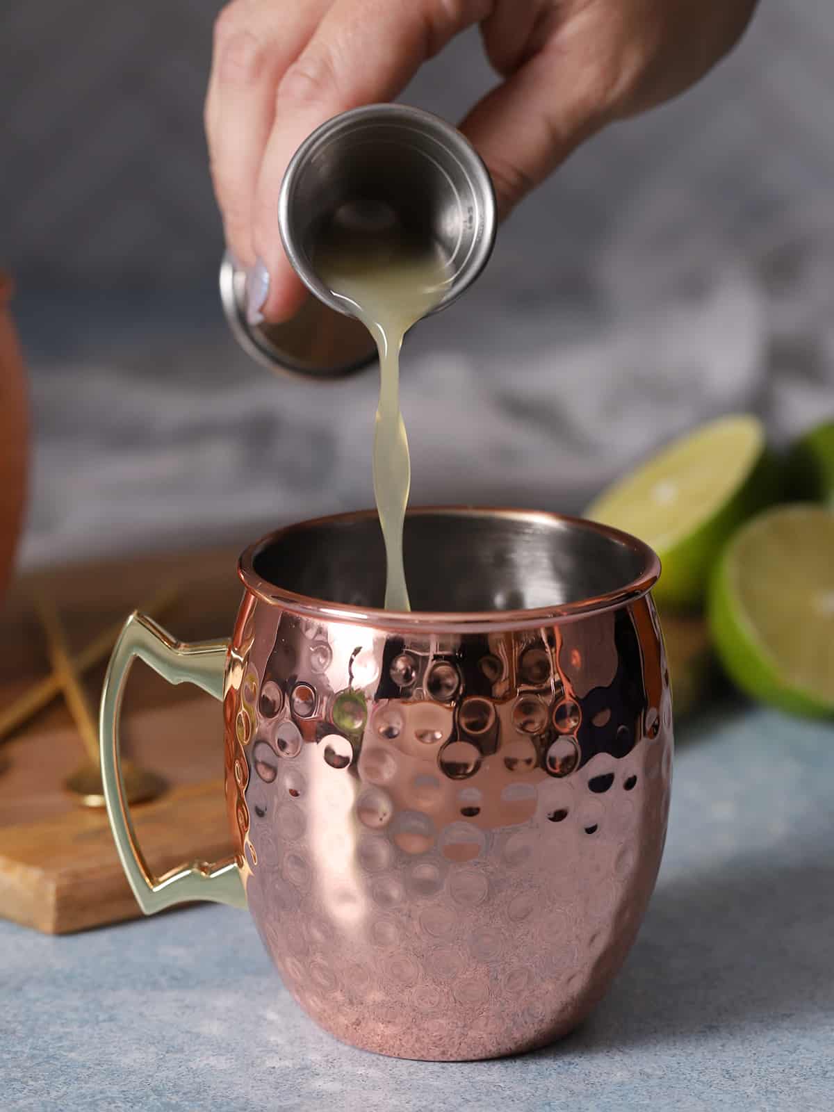 A hand pouring lime juice into a copper mug. 