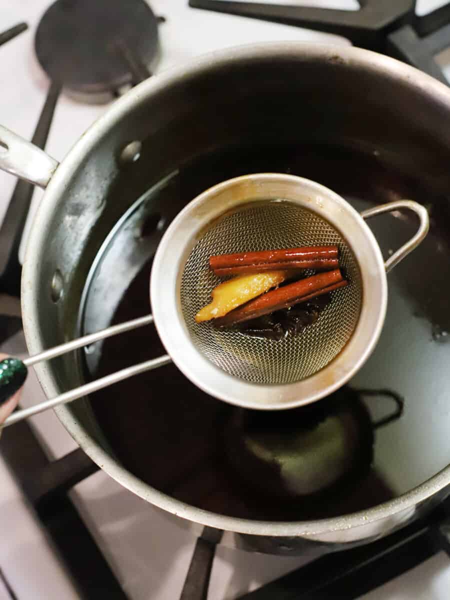 A small fine mesh strainer removing spices from the gingerbread syrup.