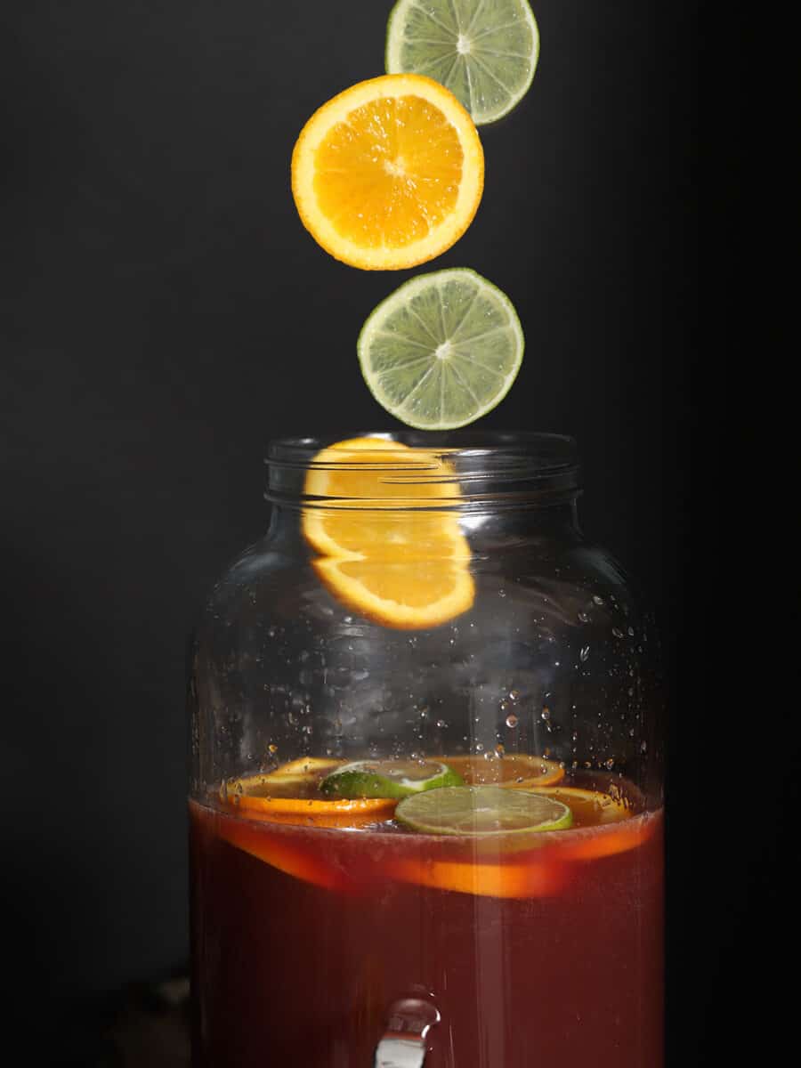 Orange slices and lime slices being dropped into a large pitcher.