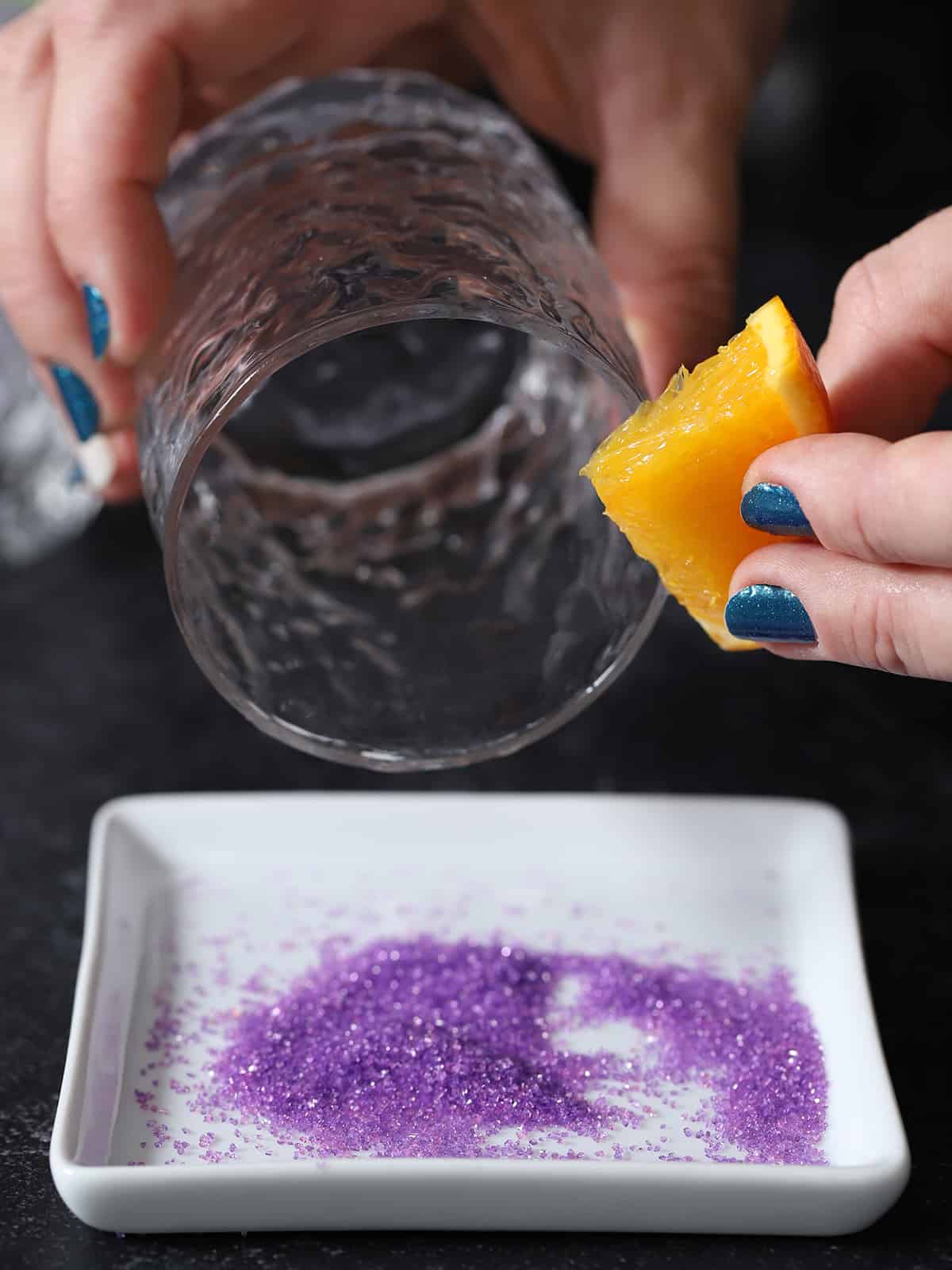 A hand holding a piece of orange up to the rim of a glass. 