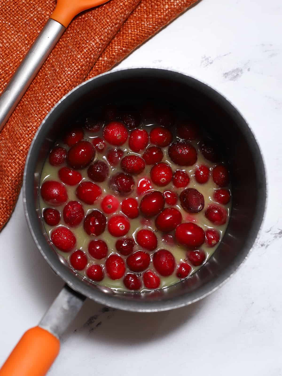 Cranberries, orange, sugar, and maple syrup in a pot. 