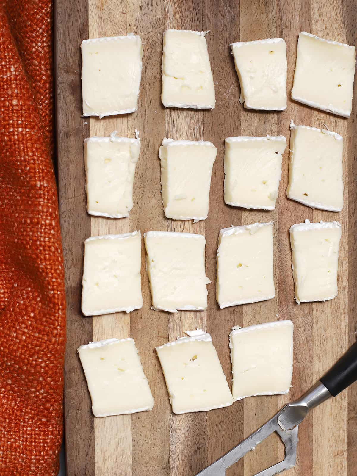 A wooden cutting board full of slices of brie cheese. 