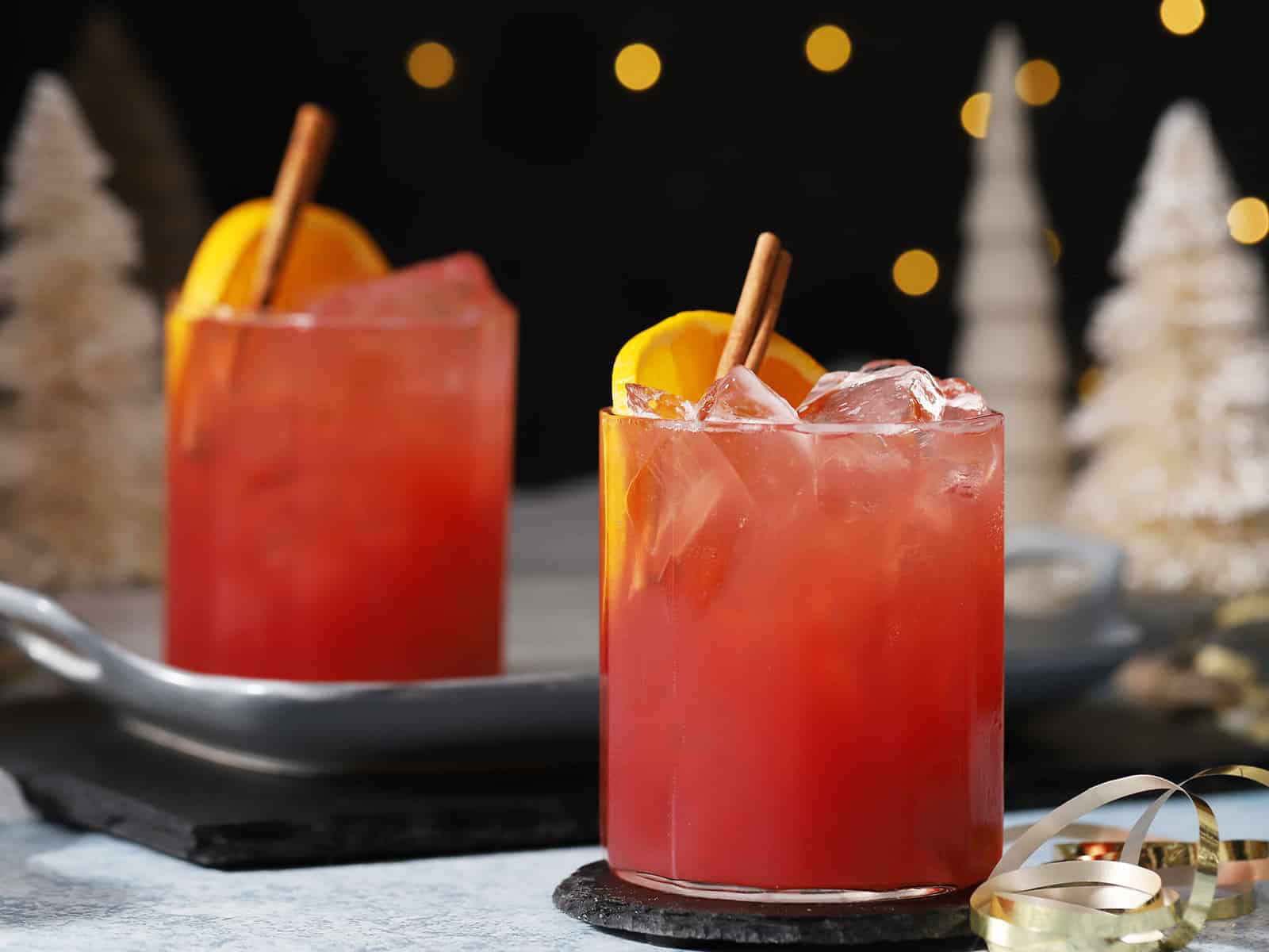 Glasses of cherry holiday mocktail garnished with orange slices and cinnamon sticks.