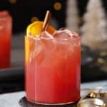 A glass of cherry holiday mocktail garnished with orange slices and cinnamon sticks.