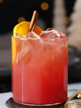 A glass of cherry holiday mocktail garnished with orange slices and cinnamon sticks.