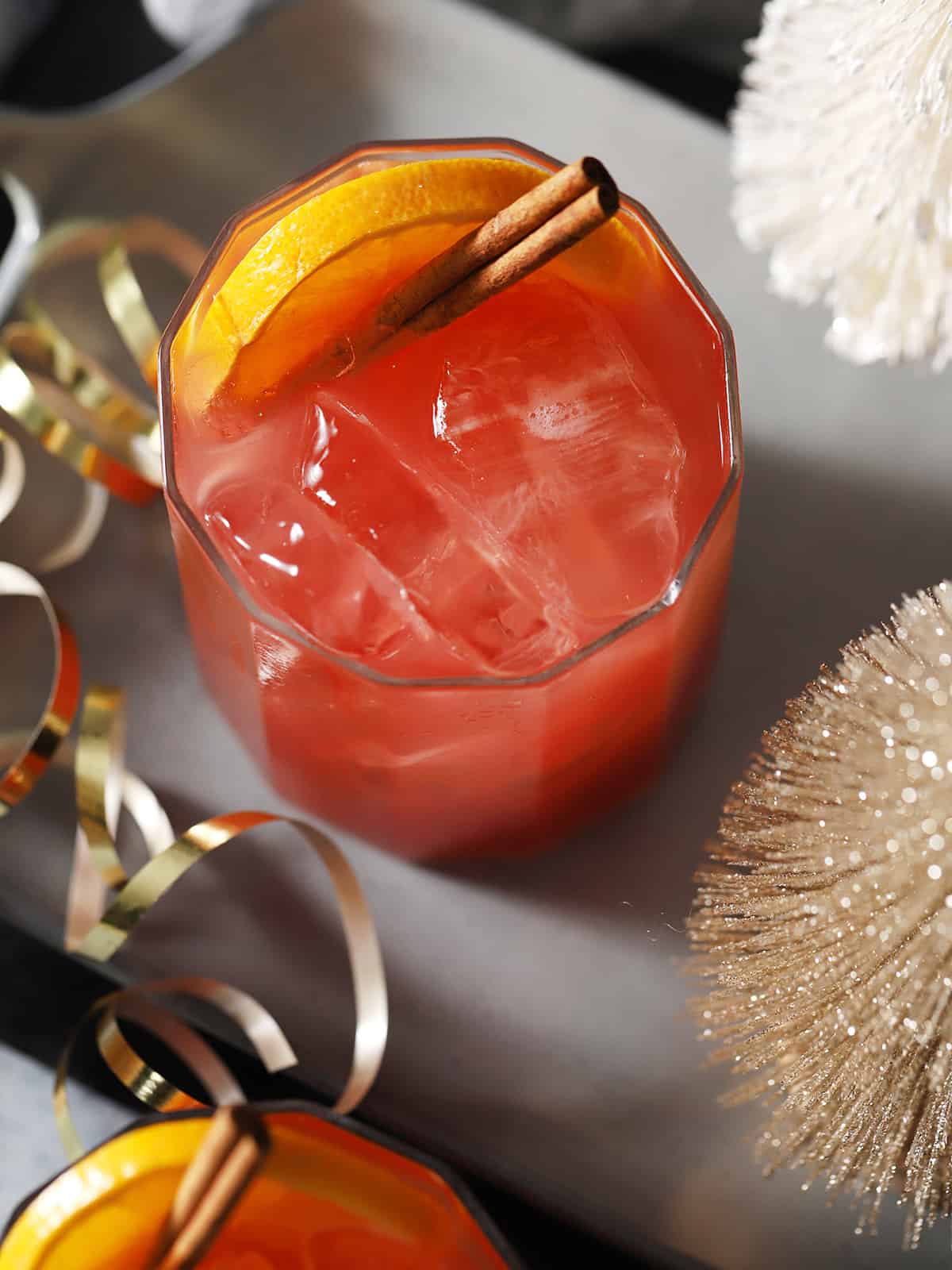 A glass of cherry holiday mocktail garnished with orange slices and cinnamon sticks.