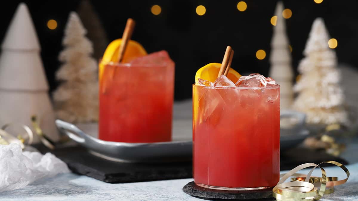 Glasses of cherry holiday mocktail garnished with orange slices and cinnamon sticks. 