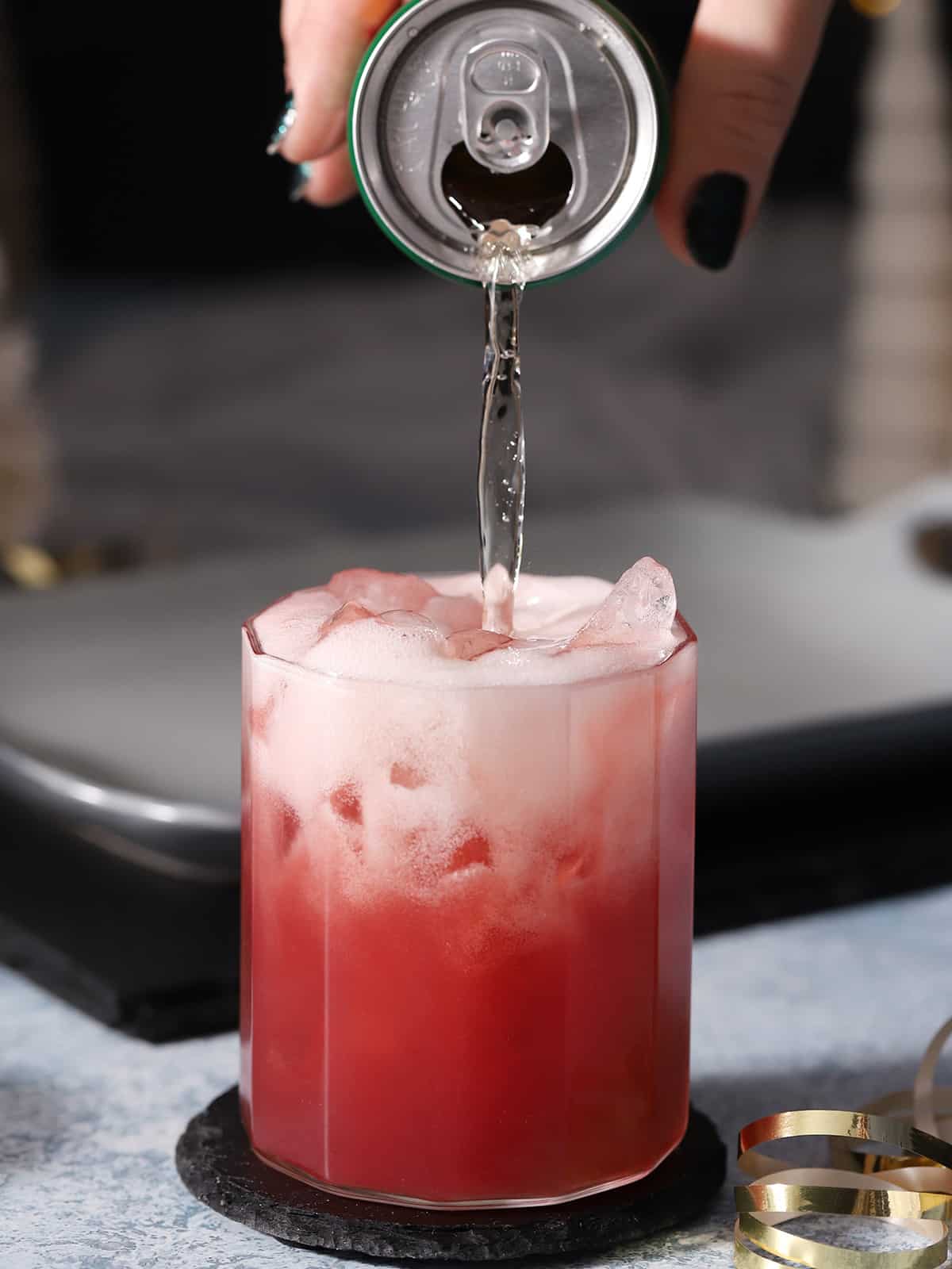 Ginger ale being poured into a glass filled with cherry mocktail. 