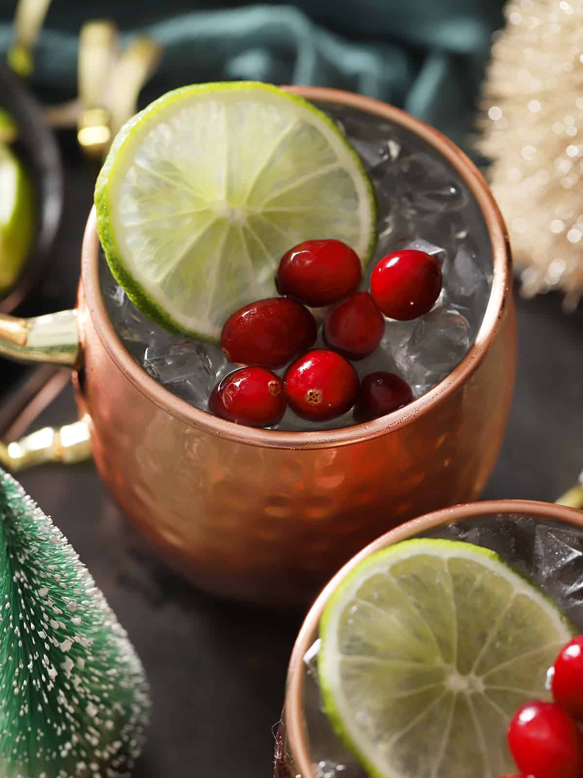 Copper mugs filled with cranberry moscow mule cocktail, garnished with lime slices and fresh cranberries.