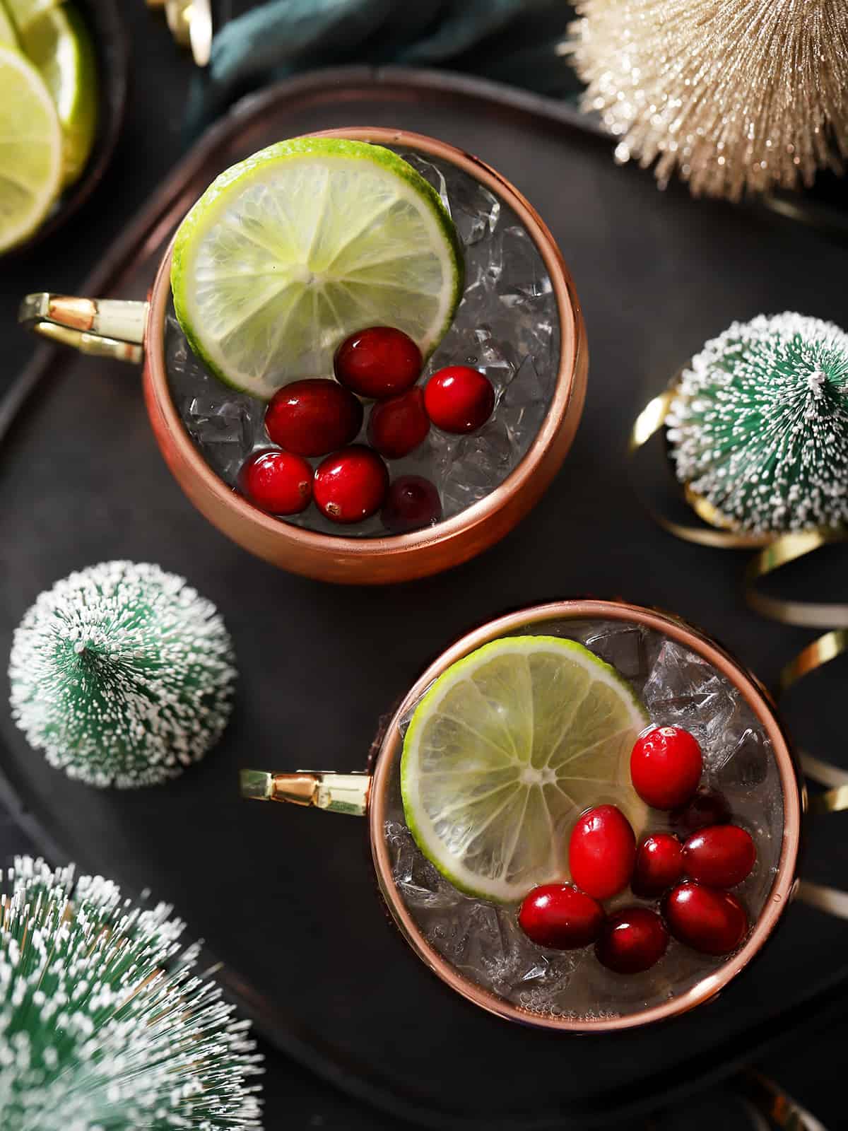 Copper mugs filled with cranberry moscow mule cocktail, garnished with lime slices and fresh cranberries.
