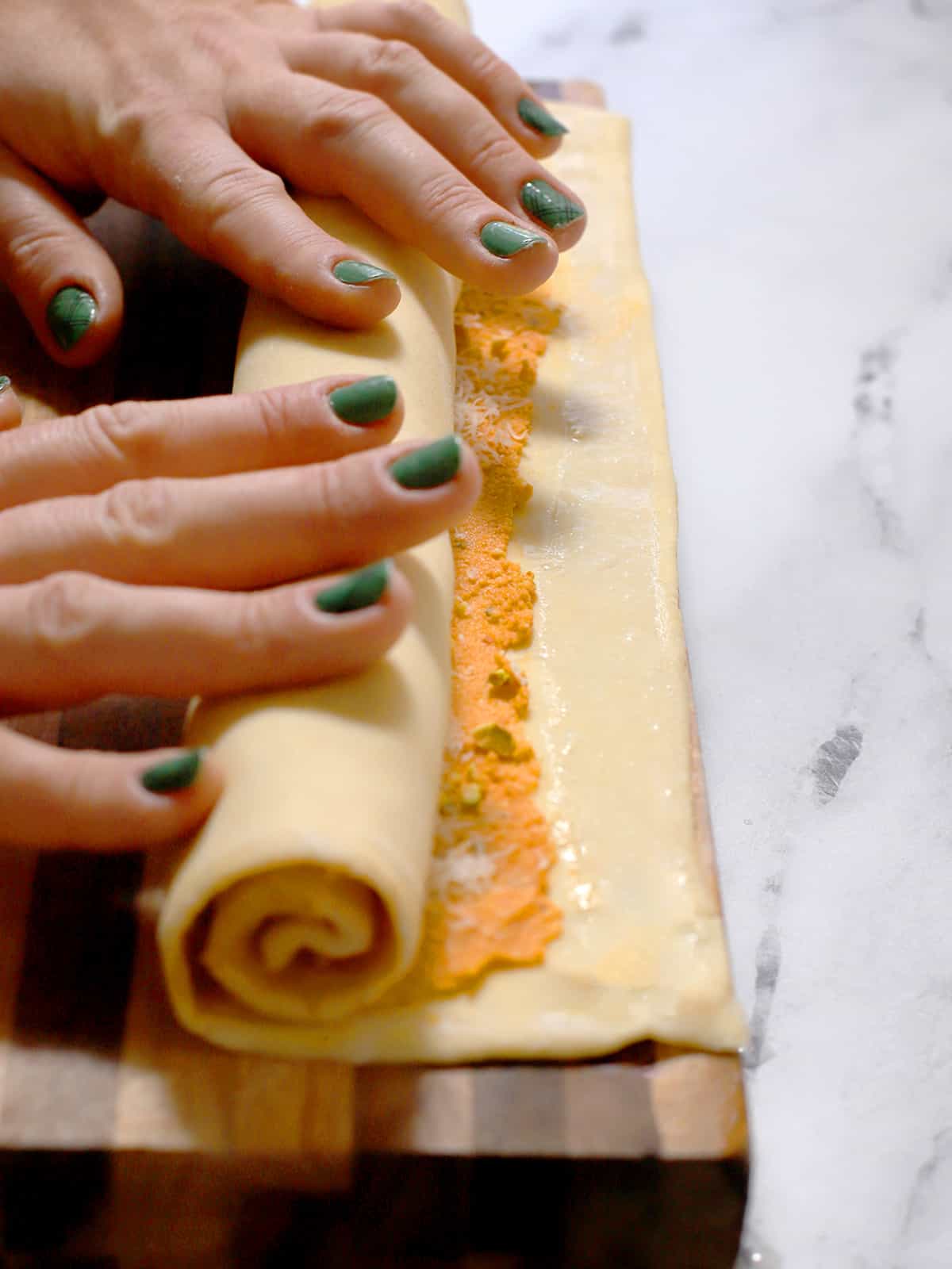 Hands rolling up the filled puff pastry. 