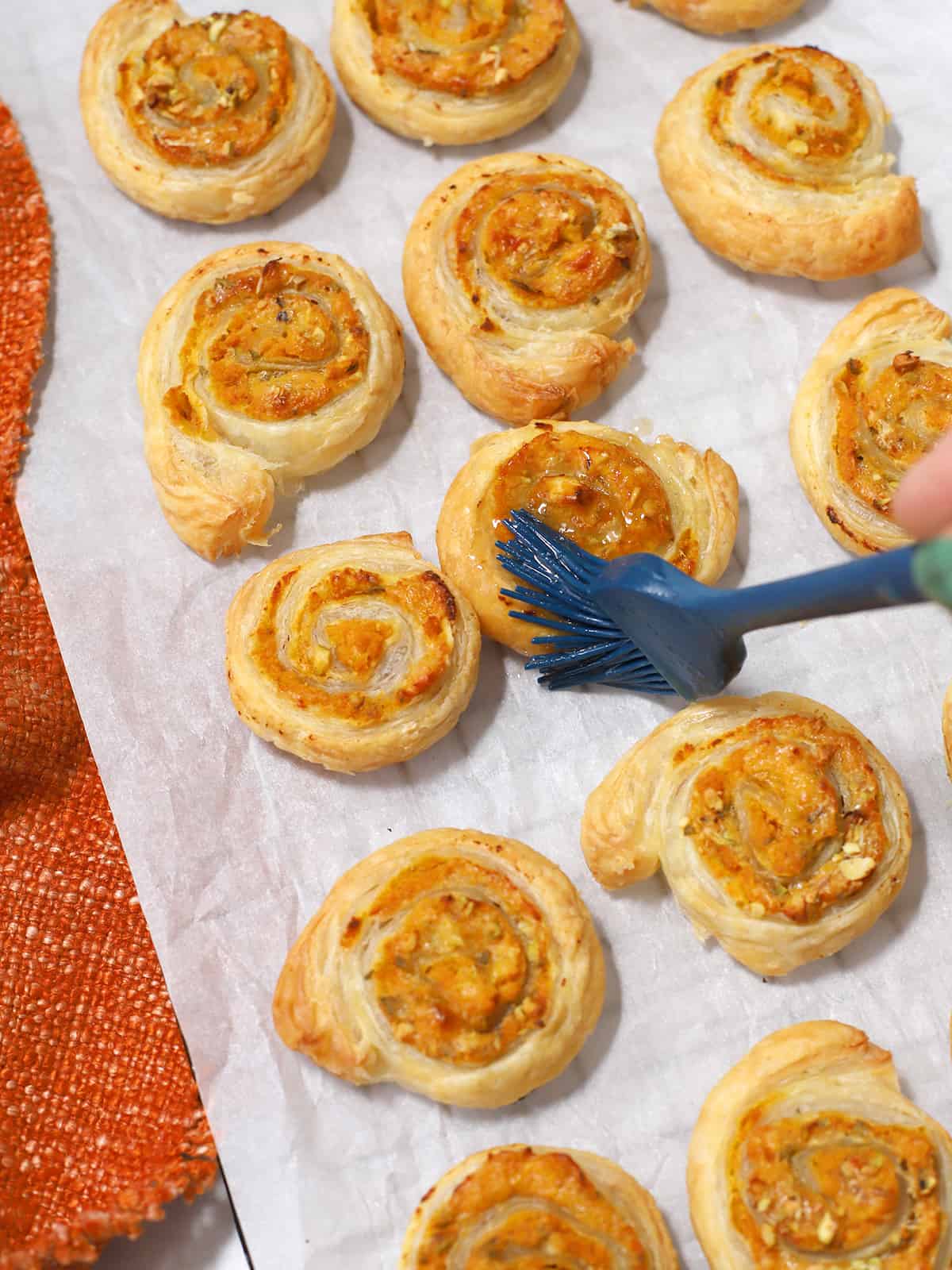 A brush covering the baked ricotta and pumpkin pinwheels with butter and syrup. 