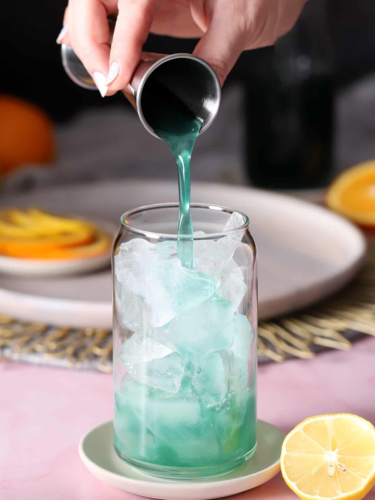 Blue curacao syrup being poured into a glass filled with ice.