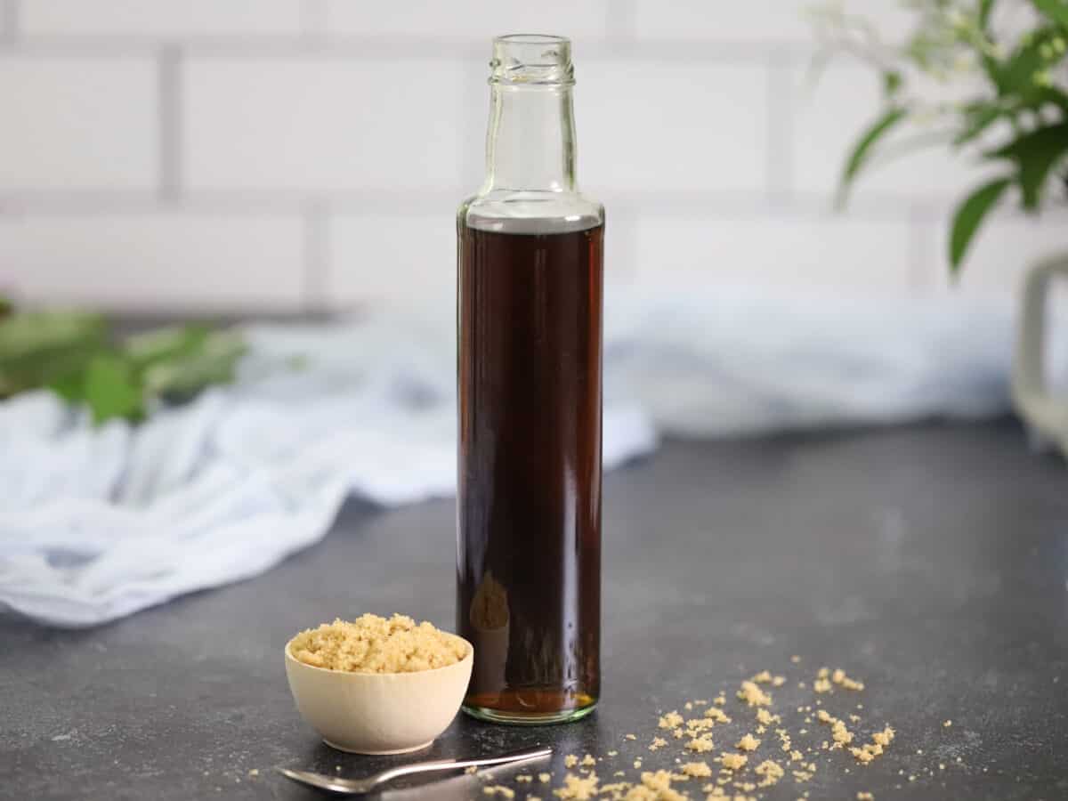 A tall bottle of brown sugar syrup with a small wooden bowl of brown sugar sitting next to it.