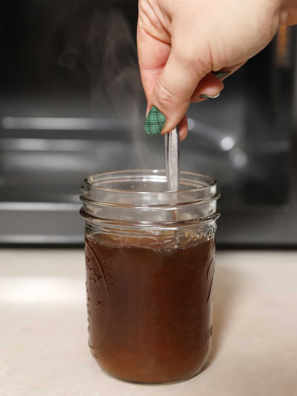 A hand stirring hot water and brown sugar in a jar. 