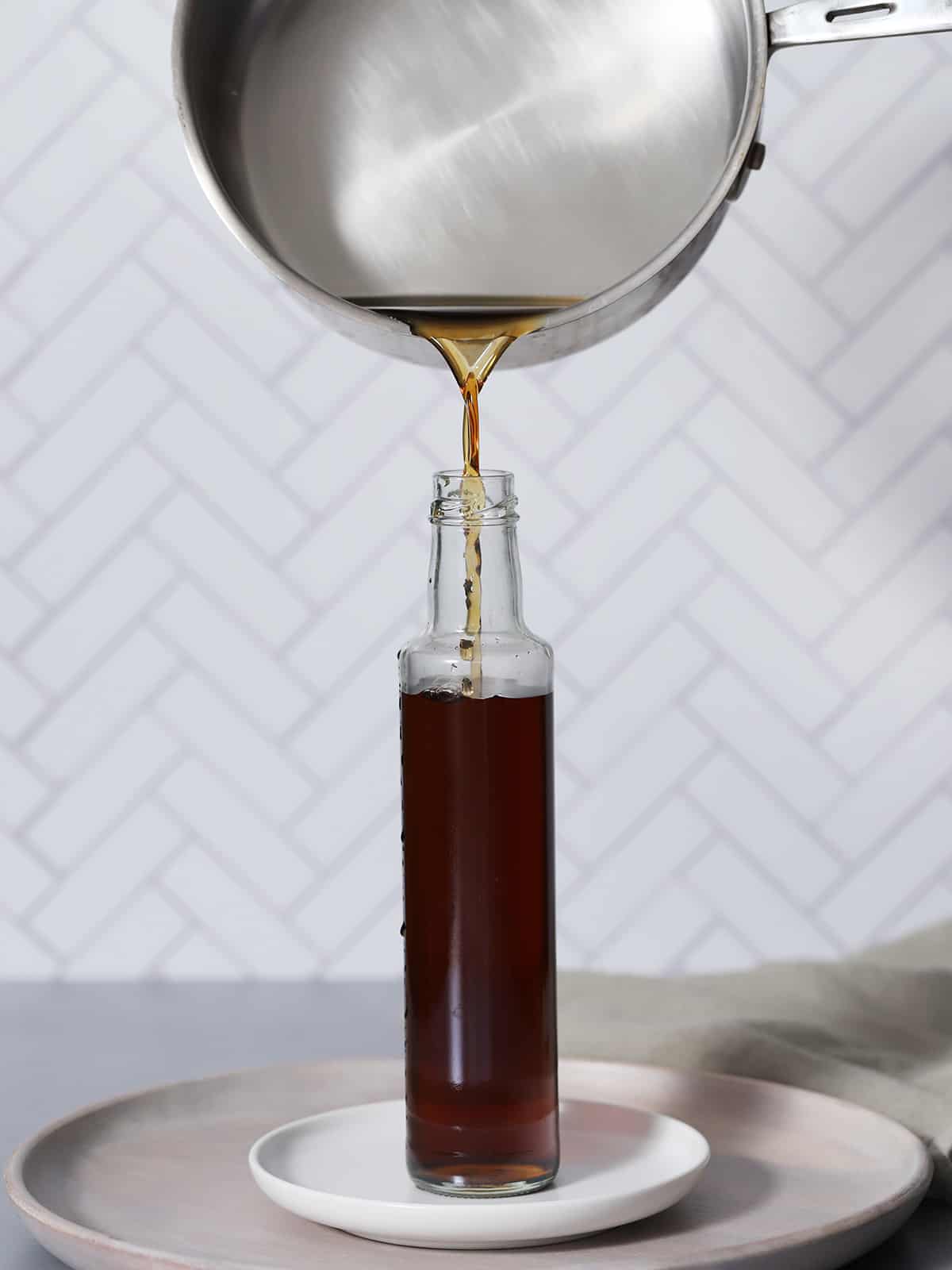 Syrup being poured from a pan into a glass bottle. 