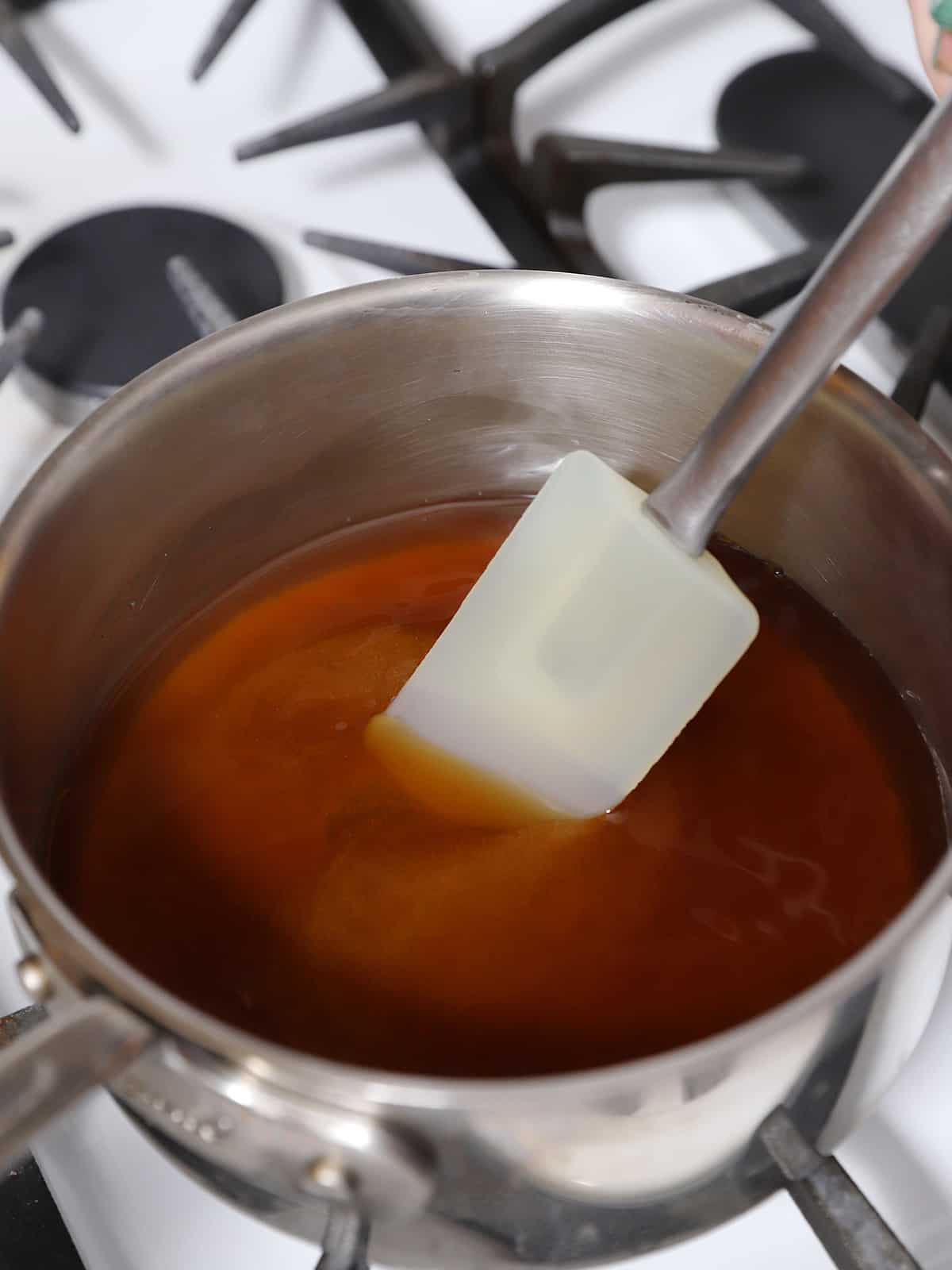 A spatula stirring a pot of brown sugar syrup. 