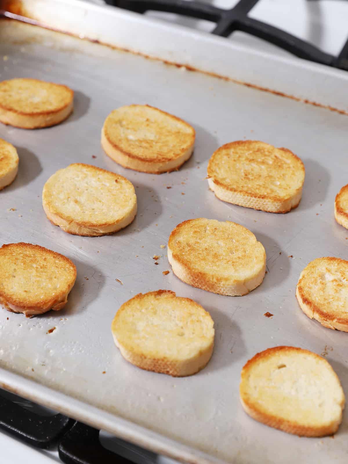 Slices of toasted French bread on a baking sheet. 