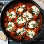 A skillet full of saucy Italian meatballs, covered in melted cheese and fresh basil.