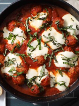 A skillet full of saucy Italian meatballs, covered in melted cheese and fresh basil.